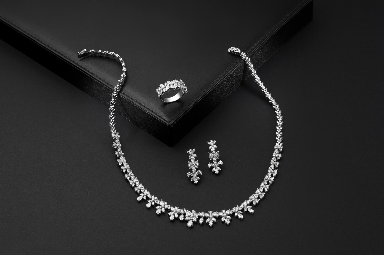 A close up of a diamond jewelry set, featuring a necklace, drop earrings and a ring, on a dark surface.