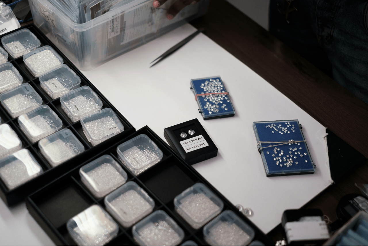 A bunch of small diamonds in different plastic containers sitting on a desk with other jewelry items and tools.