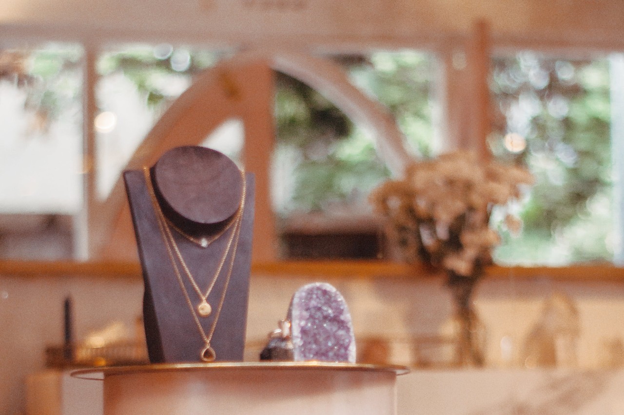 A jewelry display stand shows layered gold necklaces with round pendants inside a softly lit boutique.
