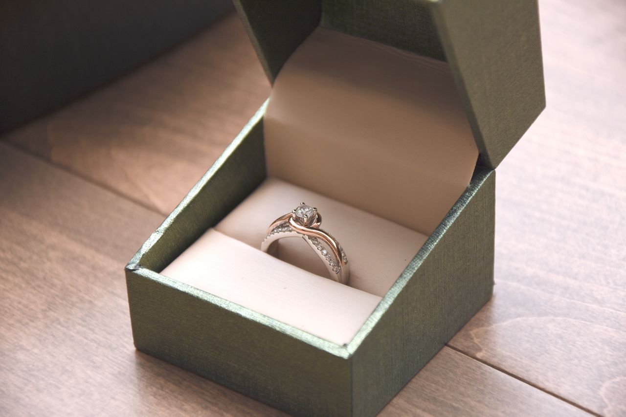 A close-up of a stunning split shank engagement ring displayed in-box atop a wooden surface. A close-up of a stunning split shank engagement ring displayed in-box atop a wooden surface.