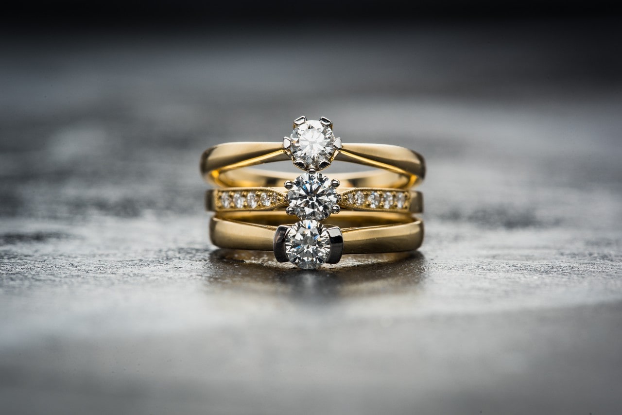 A close-up of three yellow gold solitaire engagement rings stacked one on top of the other. A close-up of three yellow gold solitaire engagement rings stacked one on top of the other.