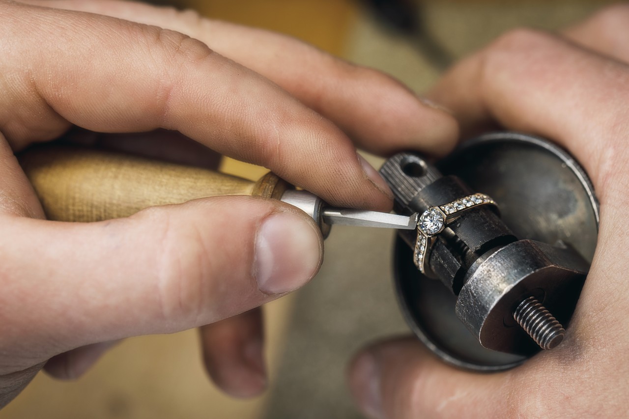 A close-up of a jeweler’s hands as they work to carefully restore a white gold ring.