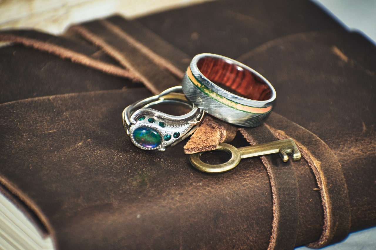A close-up of a rustic journal with a leather cover, adorned with two elegant rings and an antique brass key.
