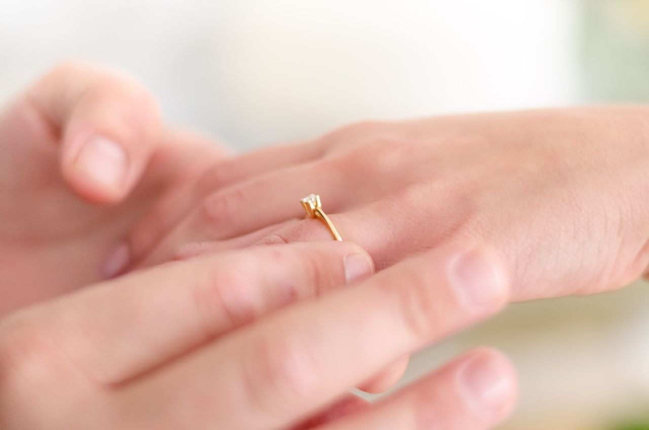 Close-up of a hand gently placing a gold engagement ring with a small diamond on another hand.
